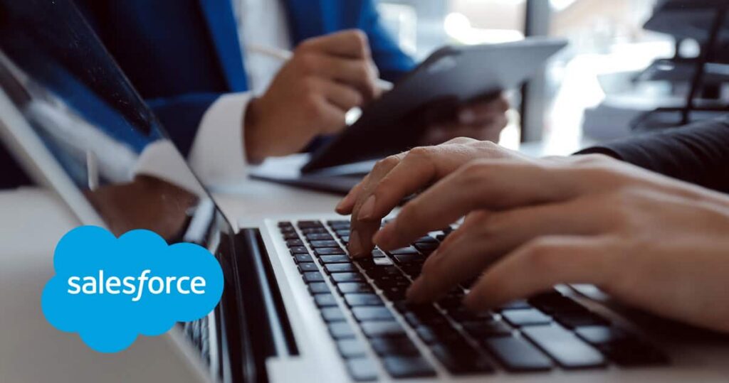 Photo of two professionals working on laptops with the Salesforce logo overlaid, representing Salesforce marketing ROI reporting and campaign attribution setup. GNW Consulting.